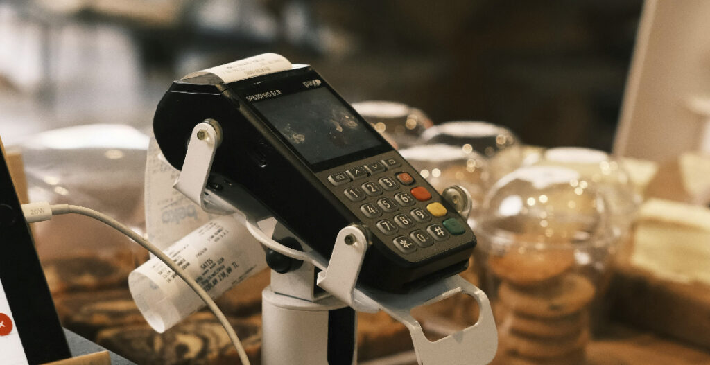 Datáfono o terminal de pago electrónico (TPV) en el mostrador de una cafetería o pastelería, listo para procesar pagos con tarjeta.